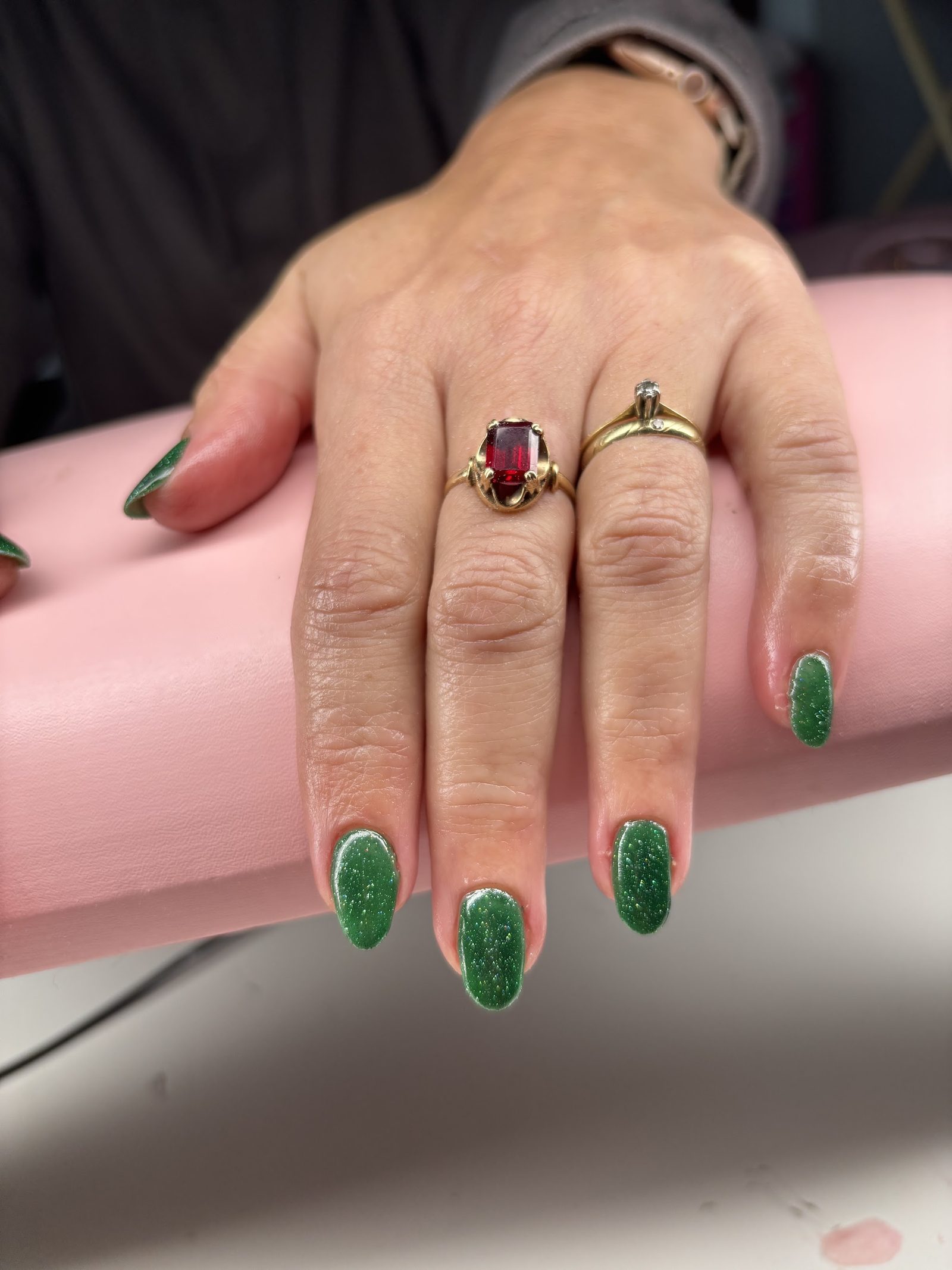 Groene glitternagels met gouden ringen op de roze handsteun