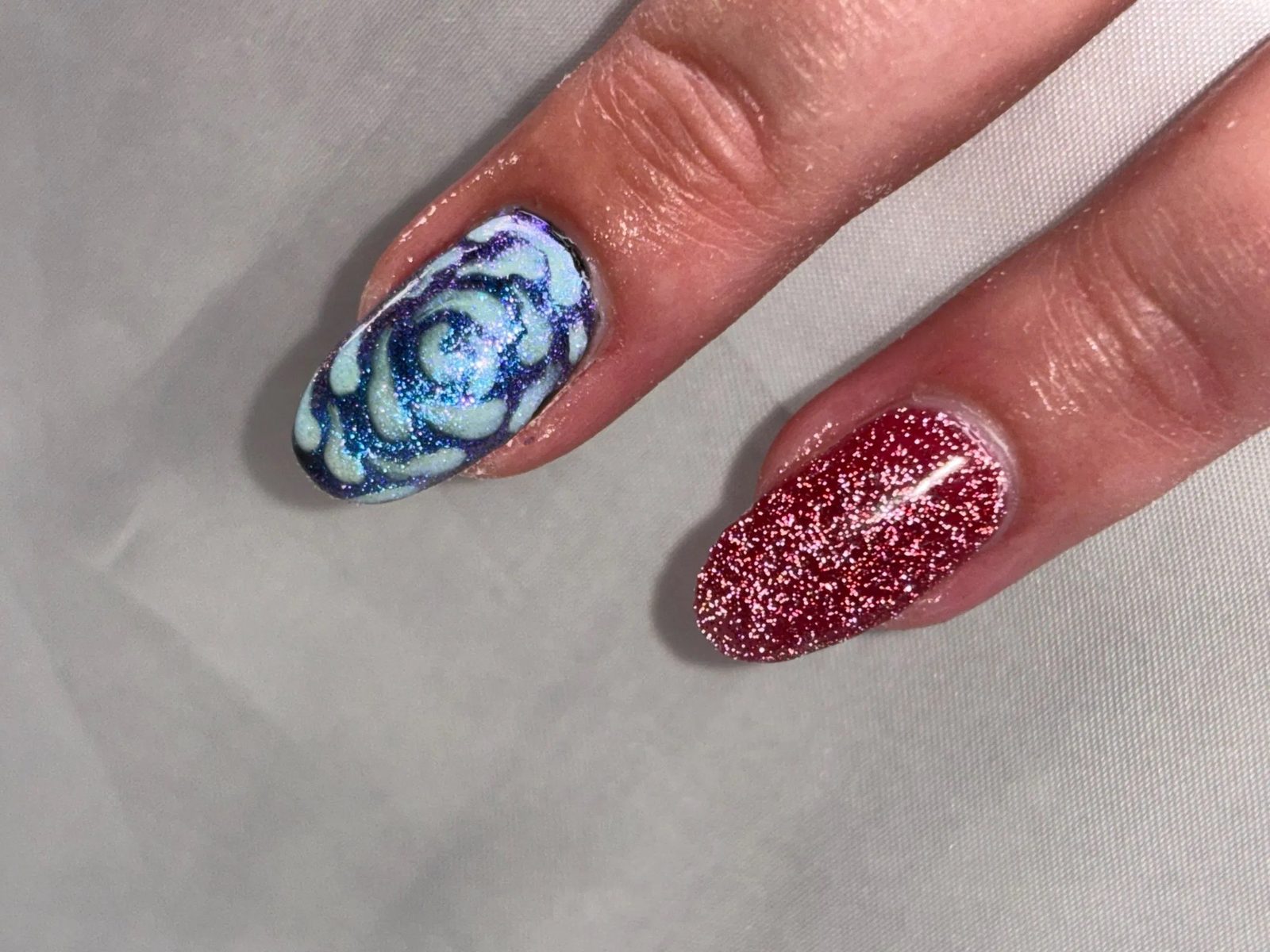 Nail art met een blauwe bloem naast een nagel met rode glitter